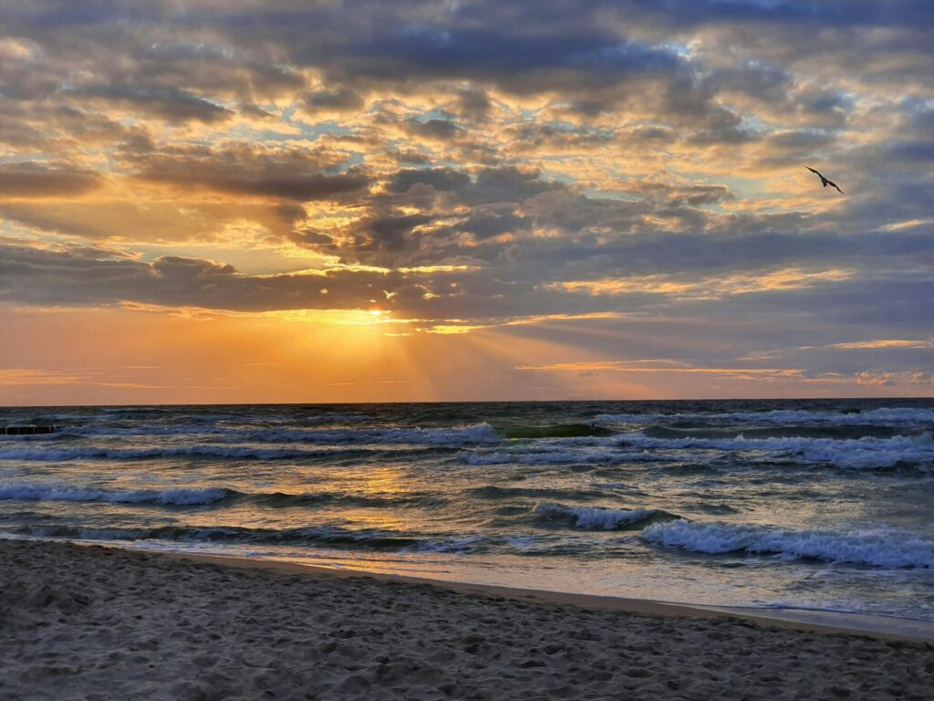 Gorgeous sunset over the ocean at Dziwnówek Beach, Poland with dramatic clouds and waves.