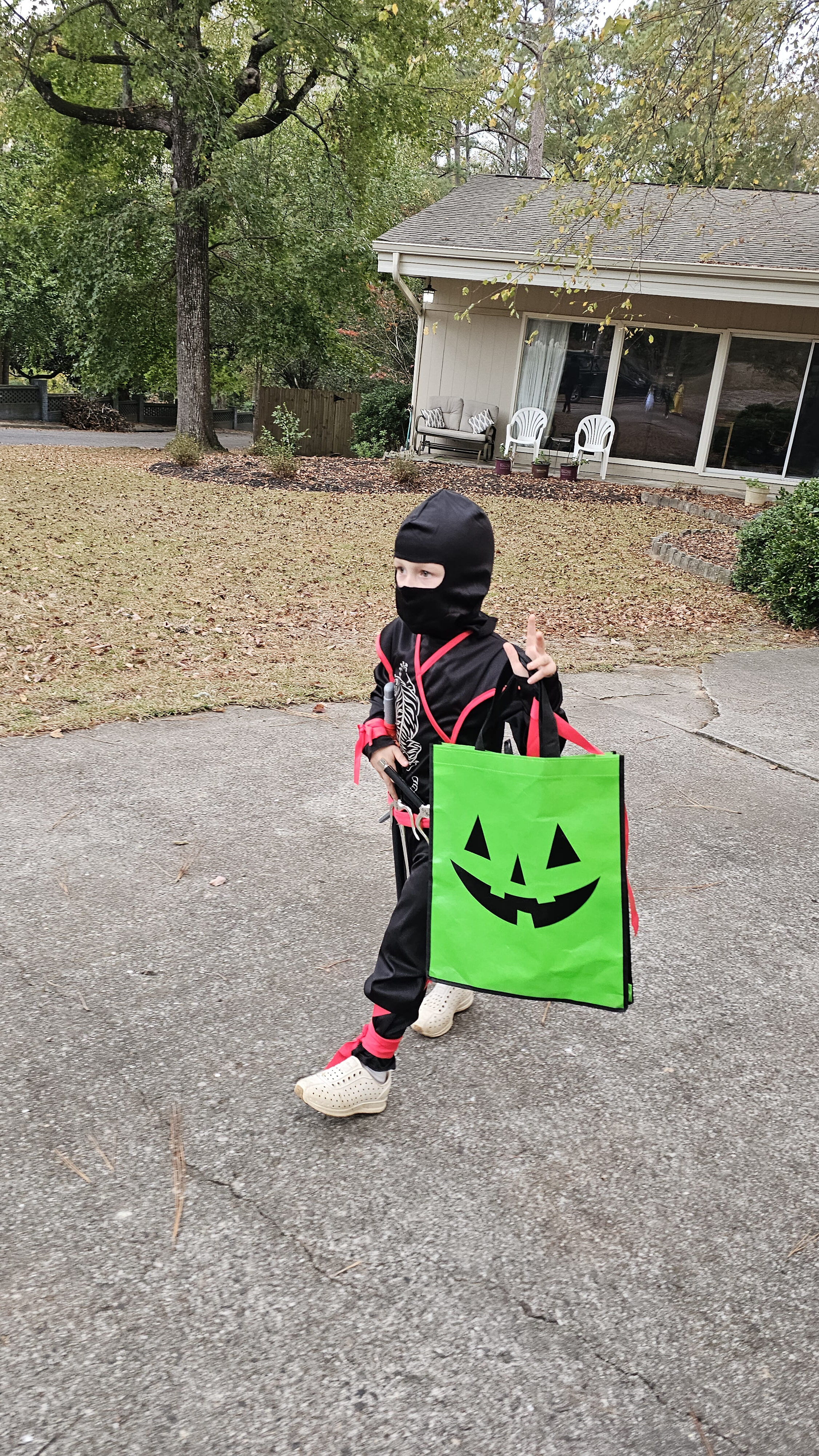 Child wearing a ninja costume and carrying a green Halloween bag