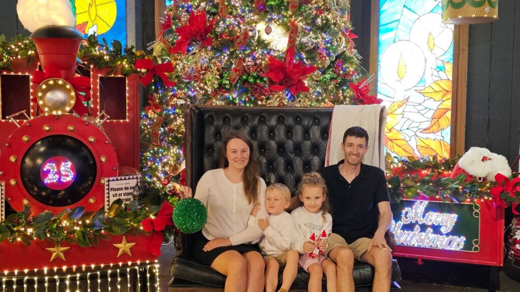 Family sitting together in front of Christmas decorations and lights during a festive holiday outing.