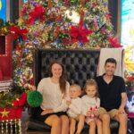 Family sitting together in front of Christmas decorations and lights during a festive holiday outing.