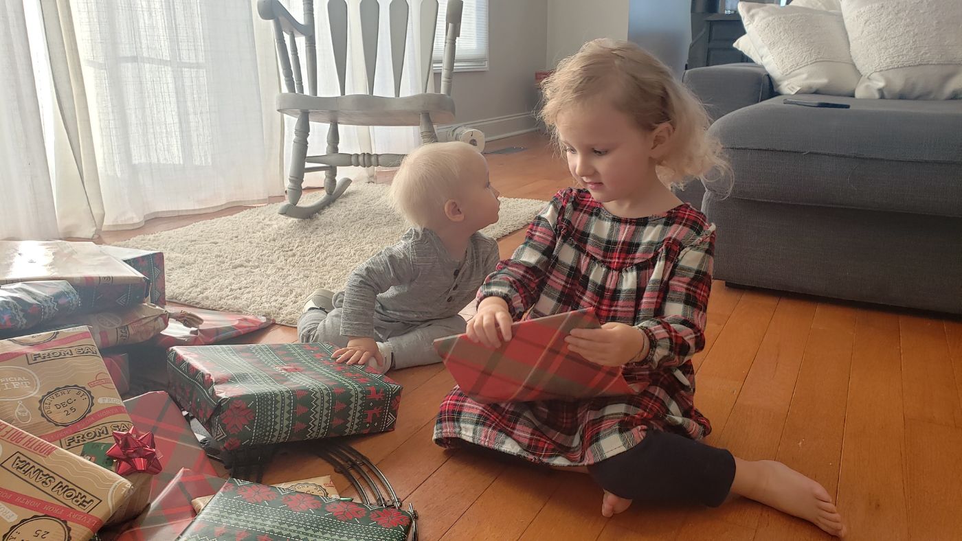 Children sitting together by wrapped Christmas presents during a cozy family Christmas morning at home.